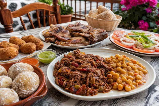 Ropa vieja, grilled pork, papas arrugadas with mojo, garbanzas, croquettes, and tomato salad on a homestyle table