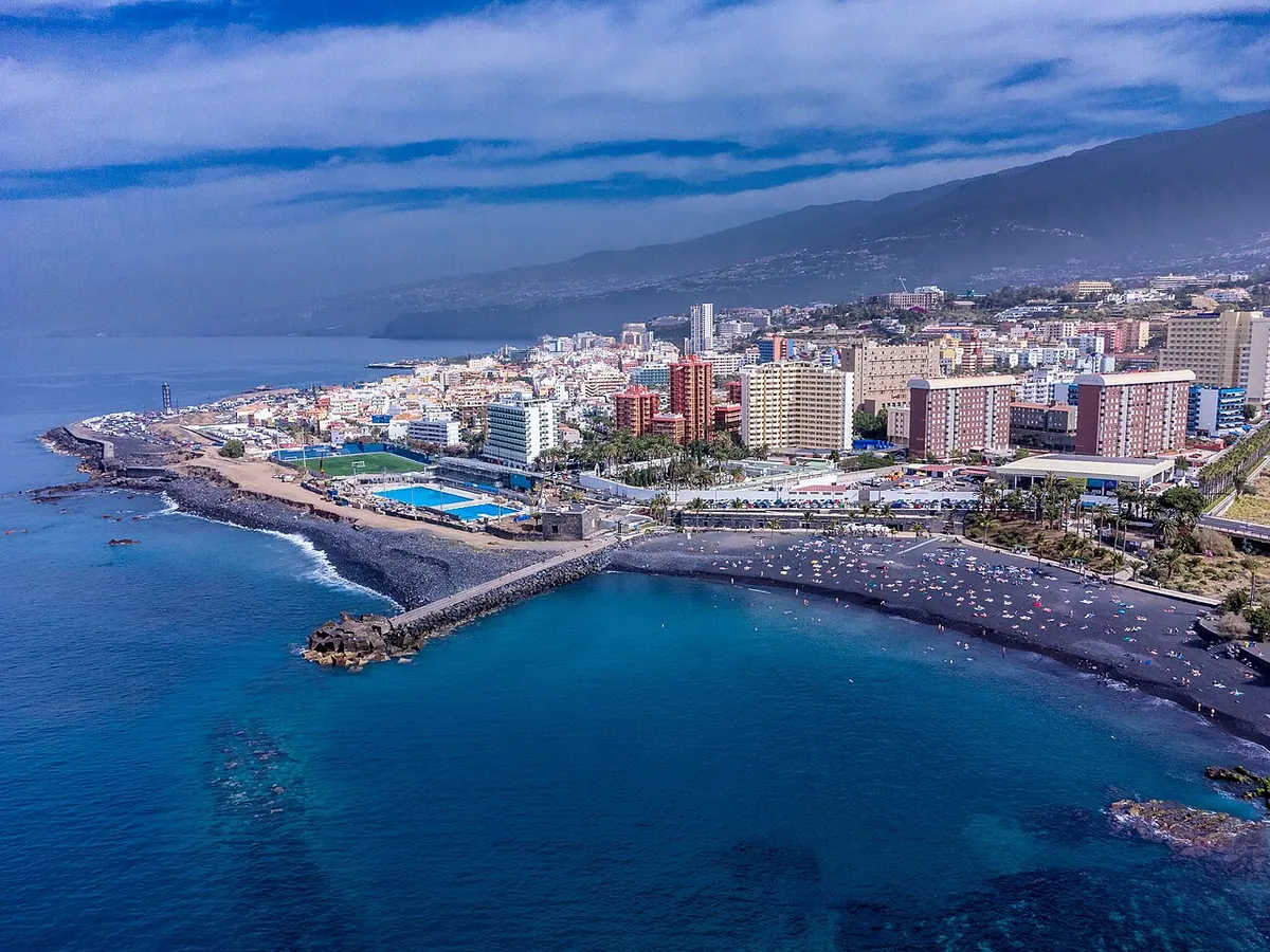 Drone view of Playa Jardin and Puerto de la Cruz behind the black-sand beach.
