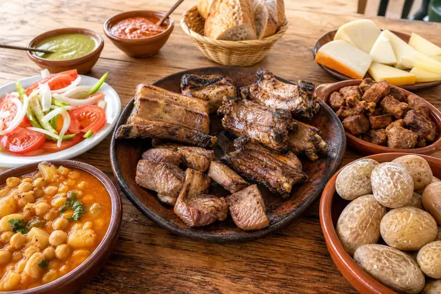 Grilled pork ribs, carne fiesta, wrinkled potatoes with mojo, local cheese, garbanza stew, and tomato salad on a rustic table