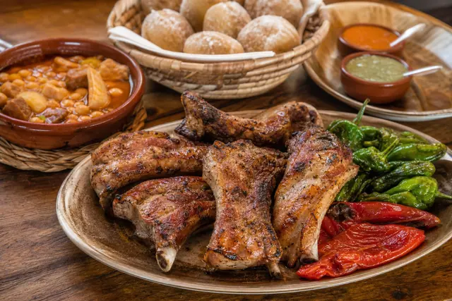 Grilled pork ribs, papas arrugadas, roasted peppers, mojo sauces, and stew on a wooden table