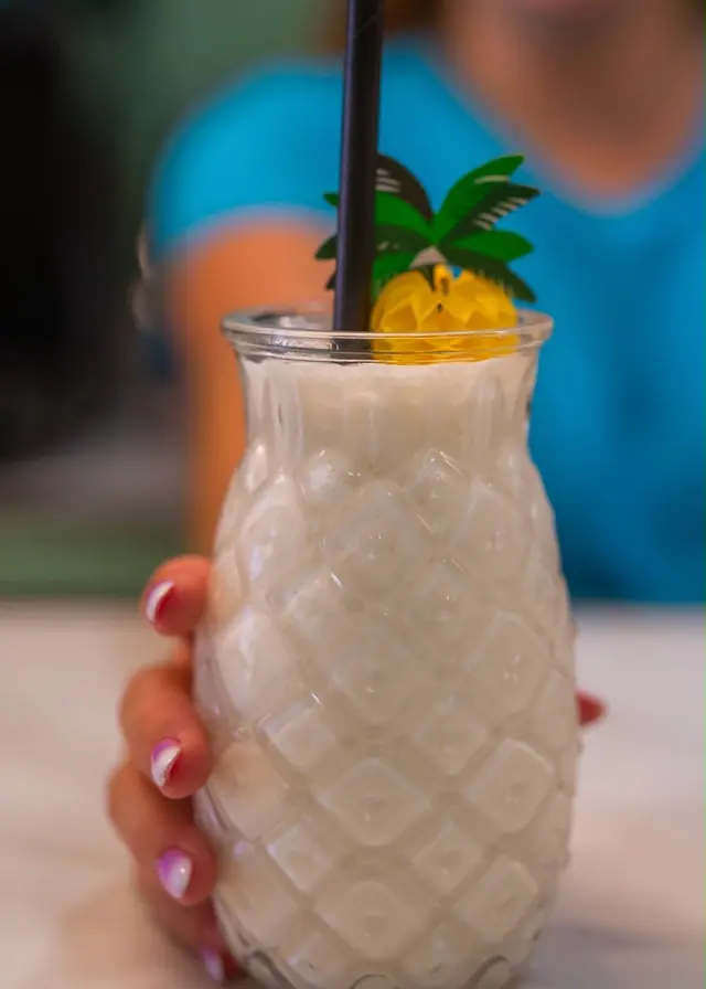 Piña Colada cocktail served in an embossed pineapple glass with decorative palm pick and black straw at Shakers, Tenerife